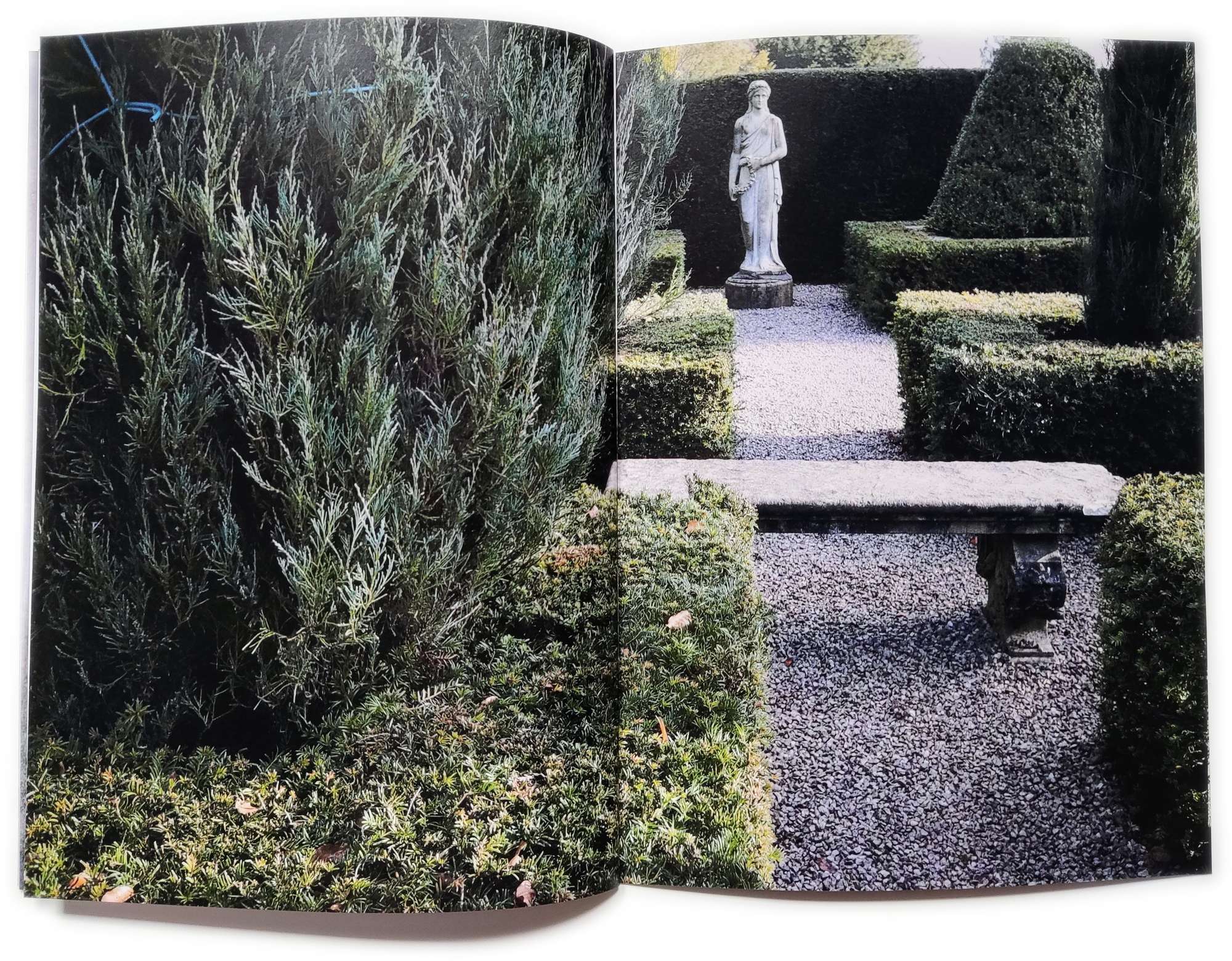 A zine full spread of an estate courtyard, marble bench and statue with hedges.